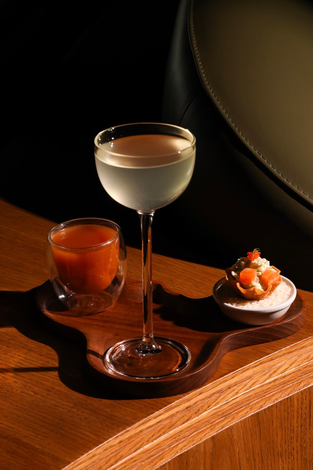 A cinematic shot of Muro’s Dirty Ceviche cocktail on a wooden tray with savory pairings, highlighting the trend of protein-forward mixology.